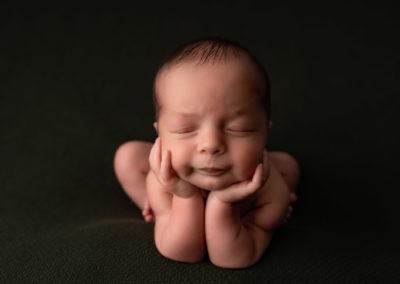 newborn photographer poses baby boy in froggy pose with face in hands