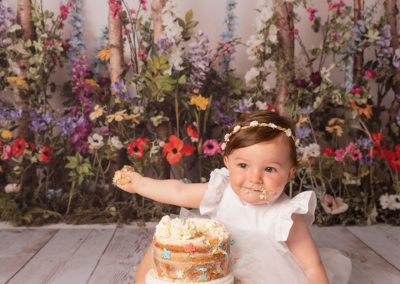 laughing with cake 1st birthday portrait of little girl in white at Cass Davies Photography cake smash studio