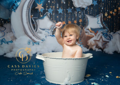happy little boy in cake smash photo shoot bath on navy background of moon and star balloons